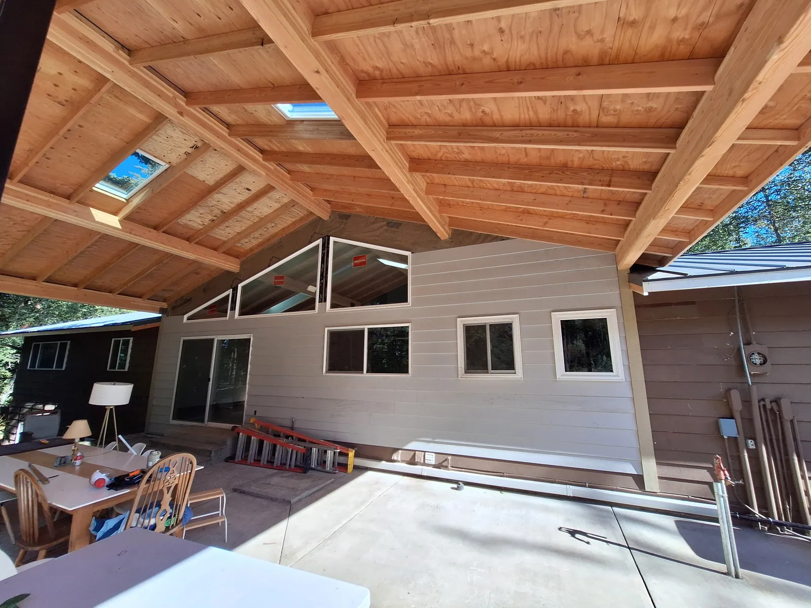 Patio cover with wood ceiling and skylights; ladder and household items remain