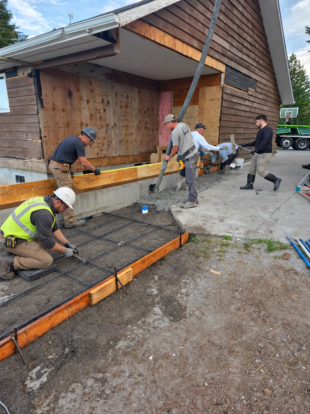 AI-enhanced review illustration of a crew placing concrete beside an existing home